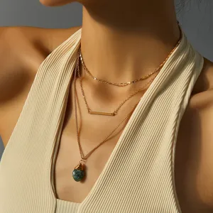 Primo piano dettagliato di collana dorata multistrato con ciondolo in pietra verde e barretta.
