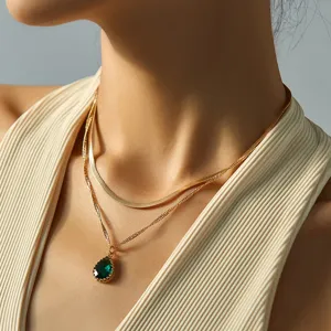 Primo piano di una collana a catena di serpente dorata a doppio strato con ciondolo verde.