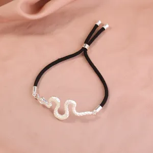 Nahaufnahme eines silbernen Schlangenanhängers an einem schwarzen verstellbaren Armband.