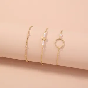 Juego de pulseras multicapa doradas con cadenas delicadas, dijes geométricos y perlas.