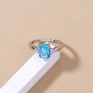 Elegante dettaglio di anello argentato con una gemma rettangolare azzurra brillante.