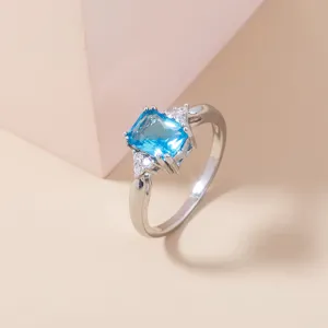 Elegante anello con zircone azzurro taglio smeraldo e pietre scintillanti sui lati.