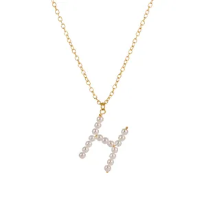 Primo piano sui dettagli del ciondolo con lettera H in perle e collana a catena dorata donna