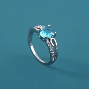 Primo piano dettagliato di un anello argentato micro-pavè con uno zircone ovale blu brillante.