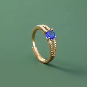 Vista dettagliata di un anello aperto dorato con pietra di zirconia blu e gambo sdoppiato.