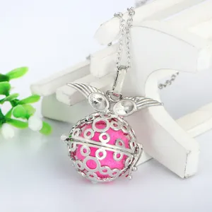 Detailed shot of angel wings locket necklace with pink diffuser ball on white prop stand.