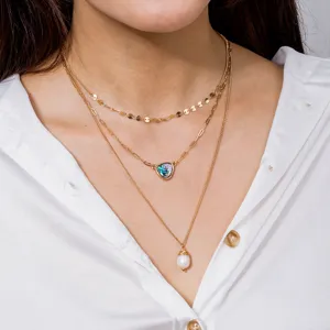 Vue détaillée du collier doré à trois couches avec pendentifs en perle et coquillage abalone.