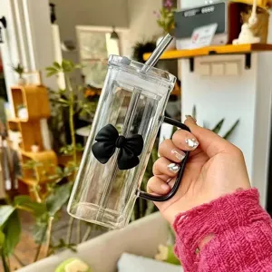 Transparent square glass cup with black bow handle and straw, aesthetic coffee milk mug.