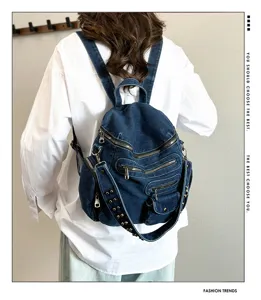 Detail view of the vintage denim backpack showing multiple zipper pockets and rivet straps.