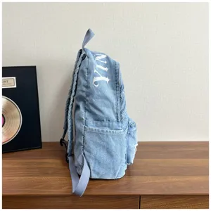 Denim backpack side view detail, washed canvas material with stylish embroidery and pockets.