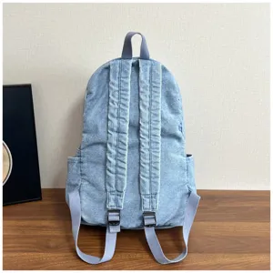 Back view of a light blue denim canvas backpack, showing adjustable shoulder straps.