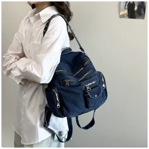 Vintage dark blue denim backpack detail with multi-zipper pockets and rivet shoulder straps.