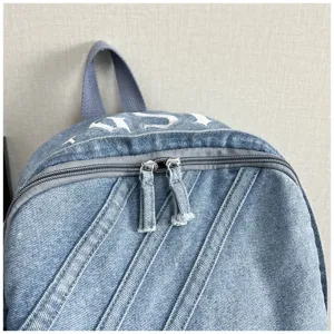 Denim backpack detail view showing washed fabric texture, durable dual zippers and top handle.