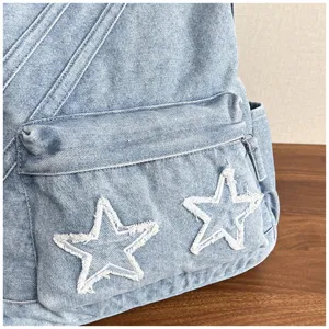 Close-up detail of a light blue washed denim backpack featuring white frayed star appliques.