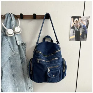Detailed view of the dark blue denim backpack hanging on a hook, featuring multiple zippers.