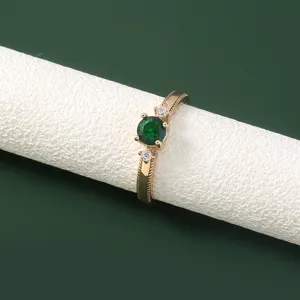 Gedetailleerde close-up van een goudkleurige ring met een groene steen en kleine zirkonia's.