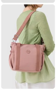 Close-up of pink nylon shoulder bag worn by model, casual tote crossbody design with straps.