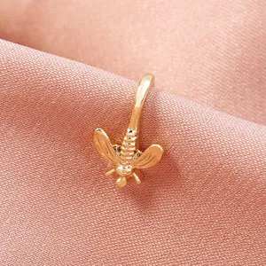 Primo piano dettagliato di un delicato anello naso ape dorato e clip per piercing su tessuto rosa.