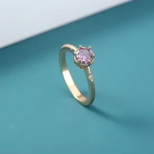 Detailopname van minimalistische vergulde ring met sprankelende paarse zirkoniasteen.