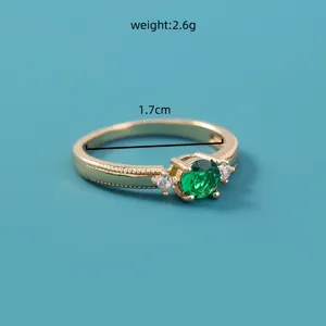 Close-up van gouden metalen ring met een levendige groene edelsteen en kleine steentjes.