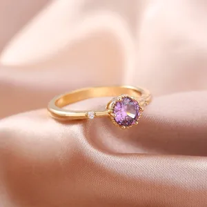 Detail van een elegante goudkleurige ring met een heldere paarse zirkoon en stenen.