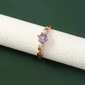 Close-up van goudkleurige ring met paarse zirkoniakristal en gedraaide banddetails.