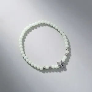 Nahaufnahme Detail eines leuchtenden Perlenarmbands mit silberner Schildkröte und Metallperlen.