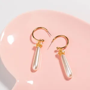 Detailed close-up of gold C-hoop earrings featuring wire-wrapped pearls and long pearl drops.