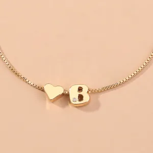 Close-up of gold box chain bracelet with heart charm and crystal letter B pendant.