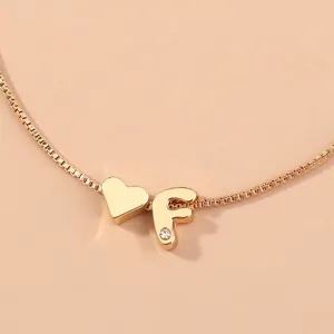 Detail shot of the gold box chain necklace featuring an elegant initial letter F and heart charm.