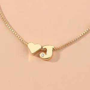 Close-up detail of gold box chain necklace featuring cute heart and rhinestone letter J charms.