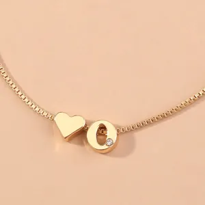 Detailed close-up of gold box chain bracelet featuring heart charm and crystal letter O.