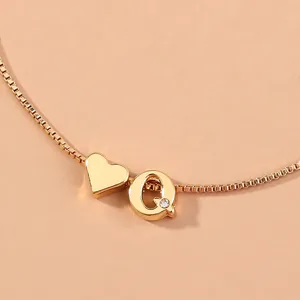 Close-up detail of a minimalist gold-plated box chain bracelet with heart and letter Q charms.