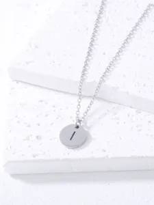 Detailed shot of a simple stainless steel round alphabet I pendant necklace on white textured block