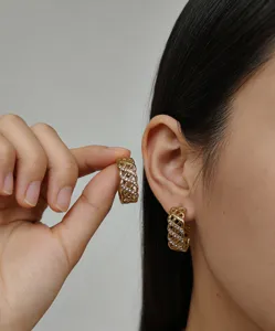 Gros plan détaillé de boucles d'oreilles créoles dorées ajourées avec incrustation de strass.