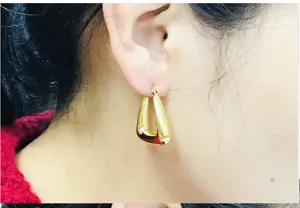 Close-up detail of geometric U-shaped gold hoop earrings worn on ear, polished finish.