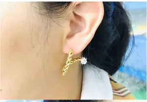 Close-up detail view of 18k gold plated twisted zircon stud earring worn on earlobe nicely.
