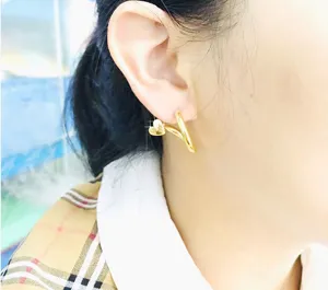 Close-up detail shot of elegant gold heart crossover earrings worn on ear, stylish jewelry.