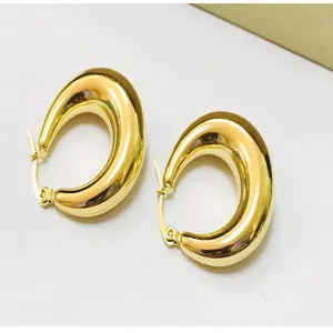 Close-up of chunky gold-toned teardrop U-shaped hoop earrings, elegant jewelry detail view.
