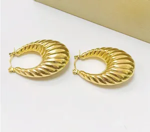 Close-up detail of chunky gold-colored ribbed croissant hoop earrings with shiny finish.