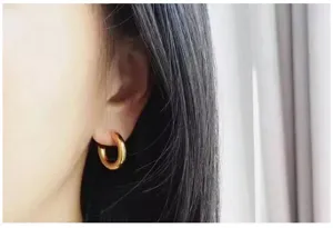Close-up of thick gold hoop earrings worn on ear, stylish and trendy metal jewelry detail.