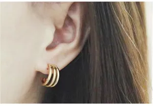 Close-up detail shot of French triple hoop C-shaped gold earrings worn on the earlobe.