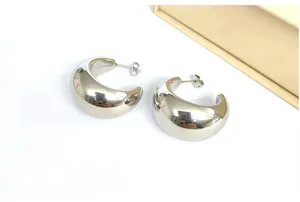 Detailed shot of chunky silver C-shaped hoop earrings, highly polished metallic finish.