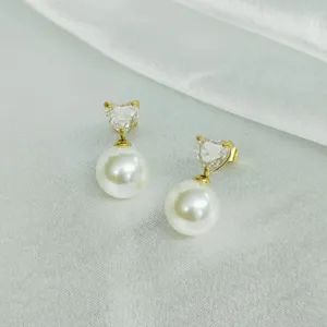 Detailed close-up of elegant heart-shaped zircon and white faux pearl dangling earrings.