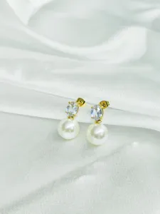 Close-up detail of elegant gold-toned zircon and faux pearl stud earrings on white silk.
