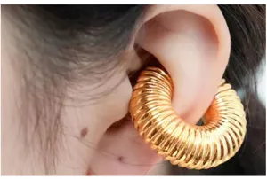 Close-up detail shot of trendy golden ribbed hollow hoop earrings worn on ear, fashionable jewelry.
