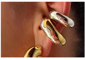 Chunky metal ear cuff detail view, showing smooth geometric design in mixed gold and silver.