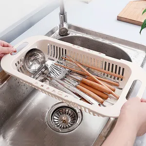 Extendable kitchen sink drain basket with utensils drying rack over stainless steel sink.