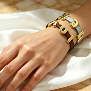 Close-up view of minimalist leather wrap bracelet featuring metallic alphabet charms on white silk.