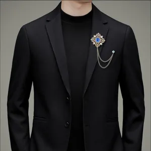 Detailansicht einer goldenen Vintage Brosche mit blauem Edelstein und Ketten am Anzug.
